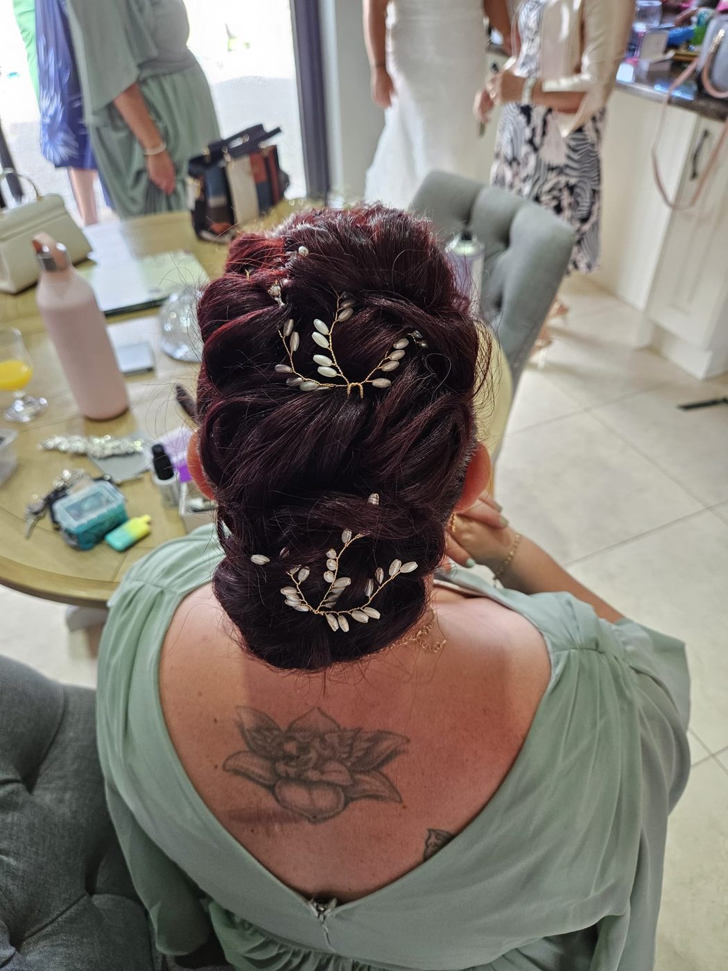 A braided burgundy updo dressed with a leaf hairpiece at INCH Hair Design